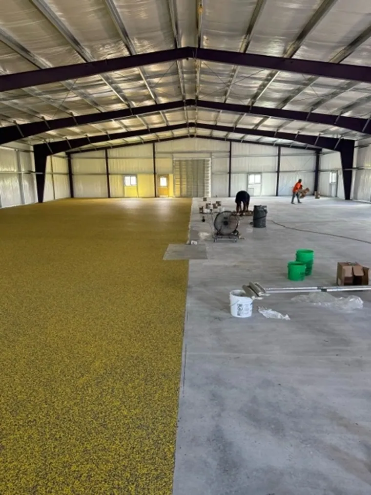 Crew broadcasting gold flake across a barn floor mid-install